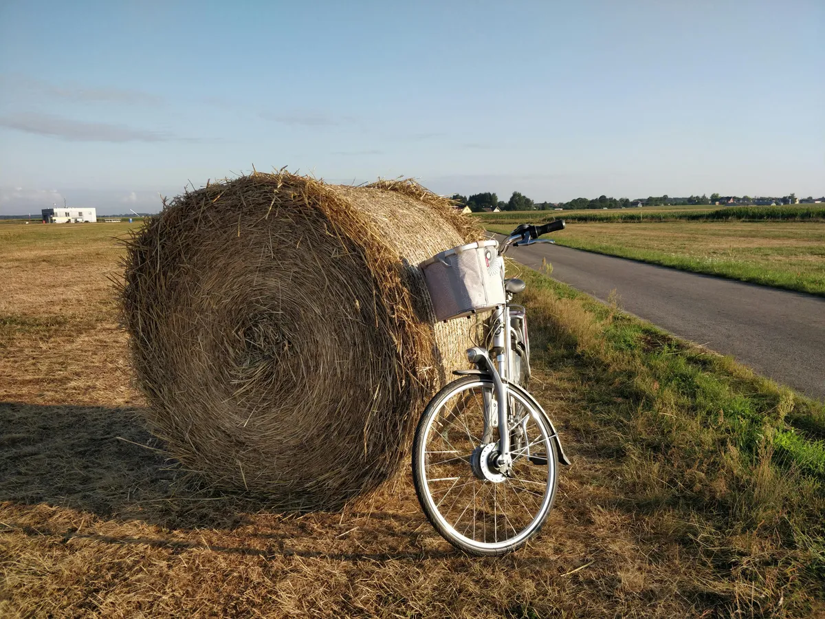 Cykel med korg parkerad vid höbal längs lantlig landsväg