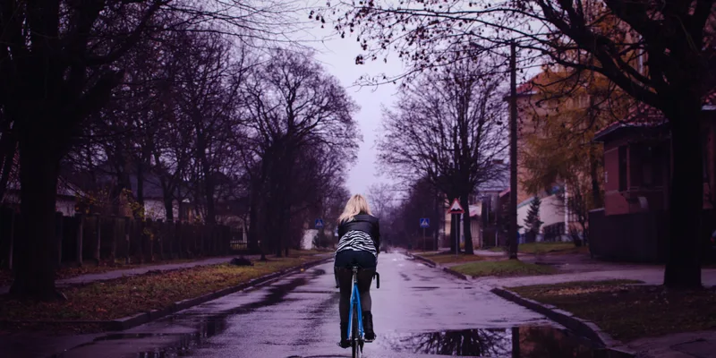 Cyklist på blå cykel på våt väg i regnigt höstväder