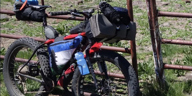 Fatbike med bikepackingväskor vid grind i naturen