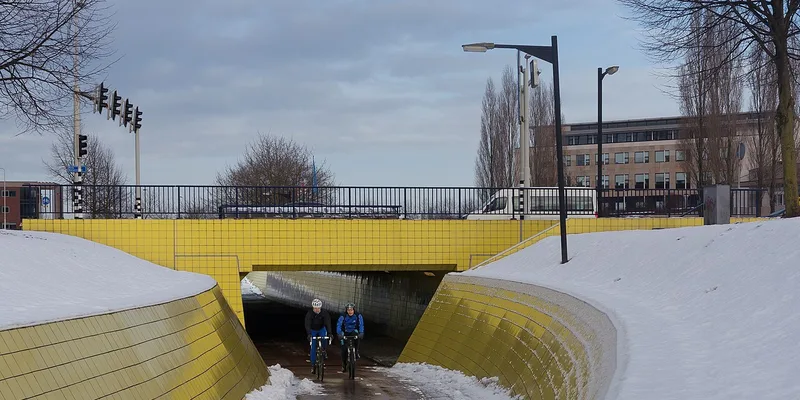 Två cyklister i snöigt vinterlandskap under viadukt