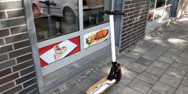 Elsparkcykel parkerad utanför butik på trottoar