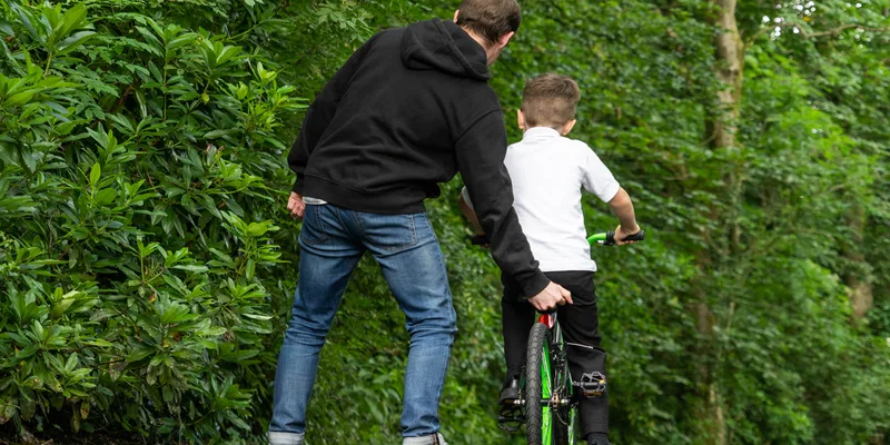 Pappa lär barn att cykla på grön stig i naturen