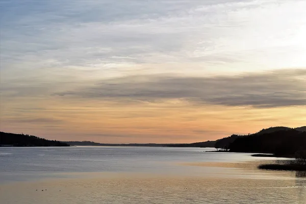 Solnedgång över sjön Åsunden med spegelblank vattenyta och skogsklädda höjder
