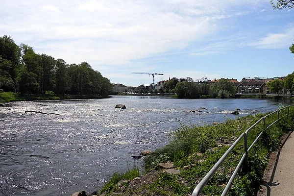 Ätran flyter bred och strömmande genom Falkenberg med strandpromenad längs vattnet