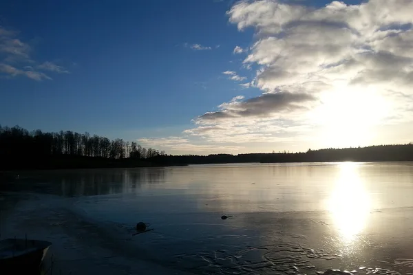 Solnedgång över isbelagd sjö med skog i bakgrunden