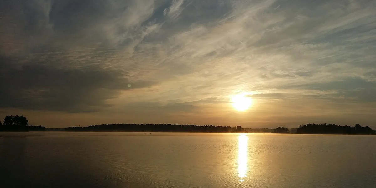 Solnedgång över stilla sjö med skogssiluett i Småland